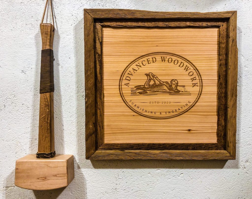 Custom wood framing of an engraved Advanced Woodwork logo with a mallet.